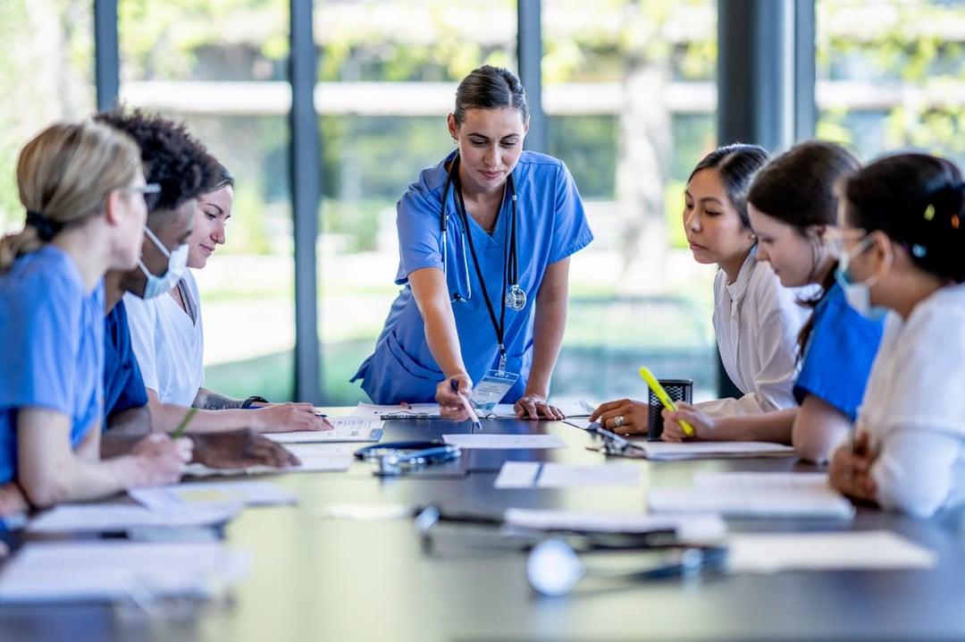 A group of pharma employees gather around a boardroom table with their team leader A group of pharma employees gather around a boardroom table with their team leader